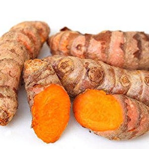 Op de afbeelding: Een verzameling verse kurkumawortels, sommige heel en andere doorgesneden om het heldere oranje binnenste te laten zien. De buitenste schil is lichtbruin met een textuur. De doorgesneden stukken tonen het heldere oranje vruchtvlees.