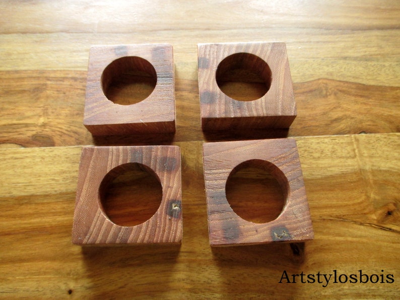 Puede incluir: Cuatro posavasos cuadrados de madera con un hueco circular en el centro. Los posavasos son de madera de color marr&oacute;n rojizo y est&aacute;n colocados sobre una superficie de madera. El texto "Artstylosbois" es visible en la esquina inferior derecha.