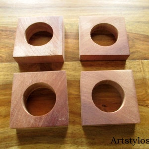 Puede incluir: Cuatro bloques cuadrados de madera con un agujero circular en el centro. Los bloques son de un color marr&oacute;n rojizo c&aacute;lido y parecen estar hechos de madera dura. Los bloques est&aacute;n colocados sobre una superficie de madera.