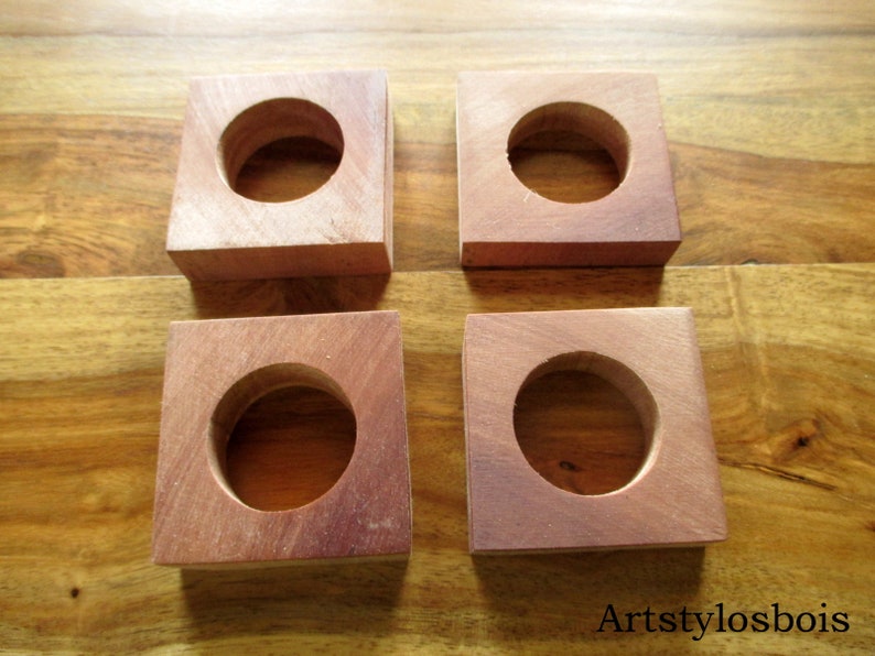 Puede incluir: Cuatro bloques cuadrados de madera con un agujero circular en el centro. Los bloques son de un color marr&oacute;n rojizo c&aacute;lido y parecen estar hechos de madera dura. Los bloques est&aacute;n colocados sobre una superficie de madera.