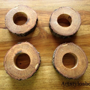 Puede incluir: Cuatro servilleteros de madera hechos de secciones transversales de una rama de &aacute;rbol. Cada anillo es de color marr&oacute;n natural con un agujero central. Los bordes de la corteza son visibles, dispuestos sobre una superficie de madera.