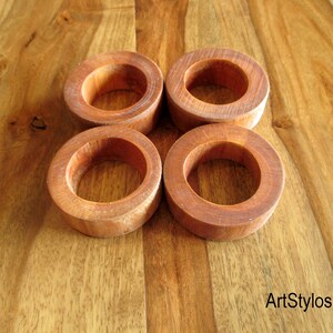 Puede incluir: Cuatro servilleteros de madera de color marr&oacute;n rojizo c&aacute;lido se presentan sobre una superficie de madera. Los anillos son circulares y tienen un acabado liso, mostrando la veta natural de la madera. El dise&ntilde;o es r&uacute;stico y elegante.