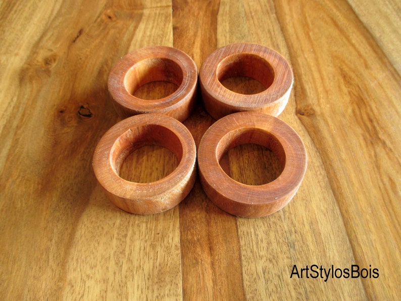 Puede incluir: Cuatro servilleteros de madera de color marr&oacute;n rojizo c&aacute;lido se presentan sobre una superficie de madera. Los anillos son circulares y tienen un acabado liso, mostrando la veta natural de la madera. El dise&ntilde;o es r&uacute;stico y elegante.