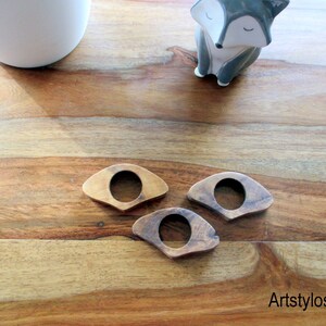 May include: Three wooden book page holders in varying shades of brown, each with a circular opening in the center. The holders are arranged on a wooden surface. A small ceramic fox figurine is in the background.