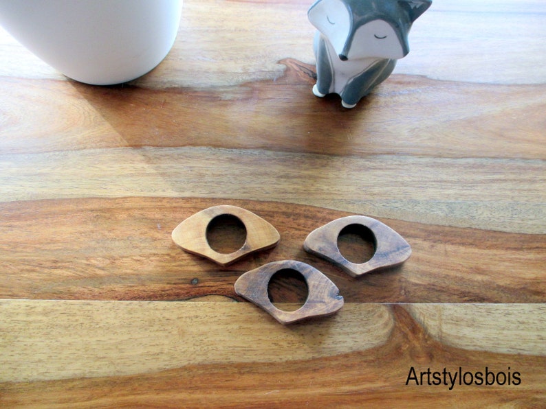 May include: Three wooden book page holders in varying shades of brown, each with a circular opening in the center. The holders are arranged on a wooden surface. A small ceramic fox figurine is in the background.