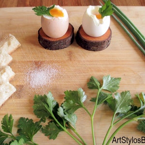 Puede incluir: Dos huevos pasados por agua, uno parcialmente pelado, sobre posavasos de madera r&uacute;stica. Perejil fresco y cebollino se disponen alrededor de los huevos sobre una tabla de cortar de madera, con rebanadas de pan y una pizca de sal.