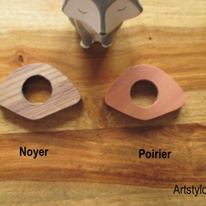 May include: Two wooden, triangular-shaped coasters with a circular hole in the center. One is made of walnut, the other of copper-colored pearwood. The word "Noyer" is printed below the walnut coaster, and "Poirier" is printed below the pearwood coaster.