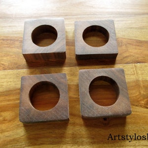 Puede incluir: Cuatro posavasos cuadrados de madera marr&oacute;n oscuro, cada uno con un agujero circular central. Los posavasos son de madera maciza y se muestran sobre una superficie de madera. Cada posavasos mide aproximadamente 7 cm.