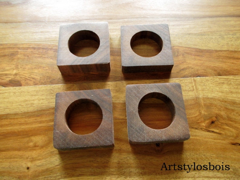Puede incluir: Cuatro posavasos cuadrados de madera marr&oacute;n oscuro, cada uno con un agujero circular central. Los posavasos son de madera maciza y se muestran sobre una superficie de madera. Cada posavasos mide aproximadamente 7 cm.