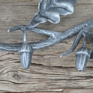May include: A silver metal oak leaf and acorn wall decor with a rustic wood background.