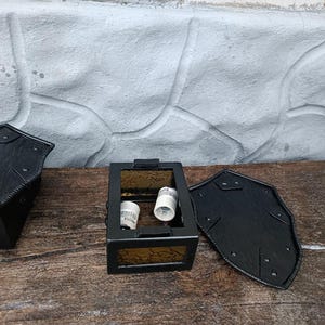 May include: Black metal lantern with amber-colored glass panels. The lantern has a rectangular shape with a hinged door and two light bulb sockets inside. The lantern is sitting on a weathered wooden surface.