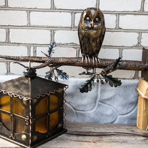 Wrought sconce in the form of an oak branch on which an owl sits with a lantern