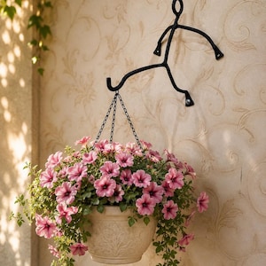 May include: A cream-coloured hanging flower pot overflowing with pink petunias and trailing green foliage. It's suspended from a black metal wall-mounted figure. The pot has an embossed design.