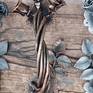 May include: A decorative metal door handle with a twisted stem and three rose-shaped accents. The handle is finished in a copper tone.