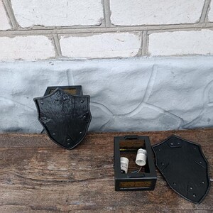 May include: Black, shield-shaped wall sconces with a textured finish. The sconces are made of metal and have a decorative design. The sconces are shown disassembled, with the electrical components visible. The sconces are on a wooden surface.