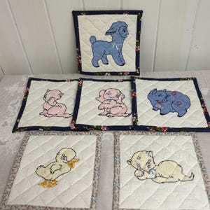 May include: A collection of quilted fabric squares with embroidered animal designs. The animals include a blue lamb, pink cat, pink dog, blue pig, yellow duckling, and a cream-colored cat. Each square has a floral border and a navy blue polka dot trim.