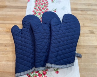 May include: Three navy blue quilted oven mitts with white and blue trim. The mitts are folded and stacked on top of each other.