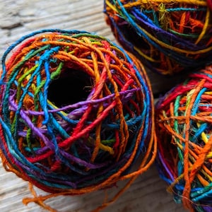 May include: Three balls of colourful yarn, each wound in a different pattern. The yarn is a mix of red, orange, yellow, green, blue, purple, and brown.
