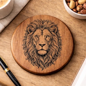 May include: Round wooden coaster with a detailed engraving of a lion's face. The coaster is brown with a natural wood grain. A black and gold pen, a cup of coffee, and a bowl of nuts are also visible.
