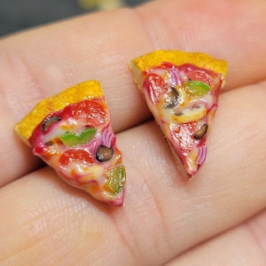 May include: Two miniature pizza slices made of polymer clay. Each slice has a yellow crust, red sauce, white cheese, green peppers, red onions, and black olives.
