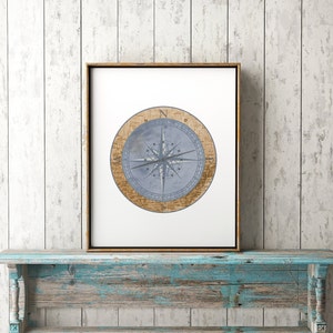 May include: A framed print of a compass with a blue and white design. The compass is surrounded by a brown circle with text. The print is hanging on a light blue wooden shelf.