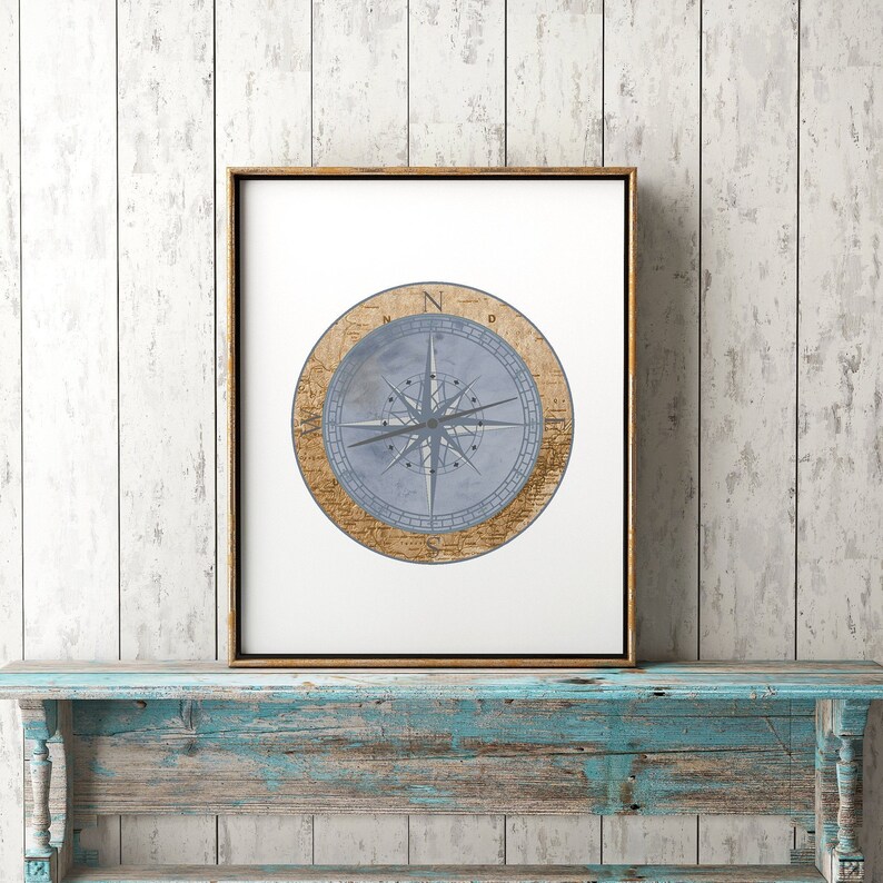 May include: A framed print of a compass with a blue and white design. The compass is surrounded by a brown circle with text. The print is hanging on a light blue wooden shelf.