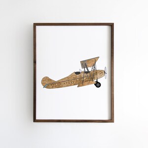 May include: A framed print of a vintage biplane with a wood grain pattern and the words "United States" printed on the side. The plane is flying against a white background.