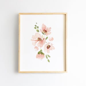 May include: A framed watercolor print featuring a cluster of delicate pink flowers with brown centers and green leaves. The artwork is set against a white background and framed in a light wood frame, creating a soft and elegant aesthetic.
