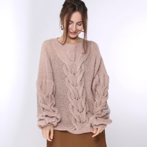 May include: A soft, blush-colored knitted sweater with a cable knit pattern and a relaxed fit.