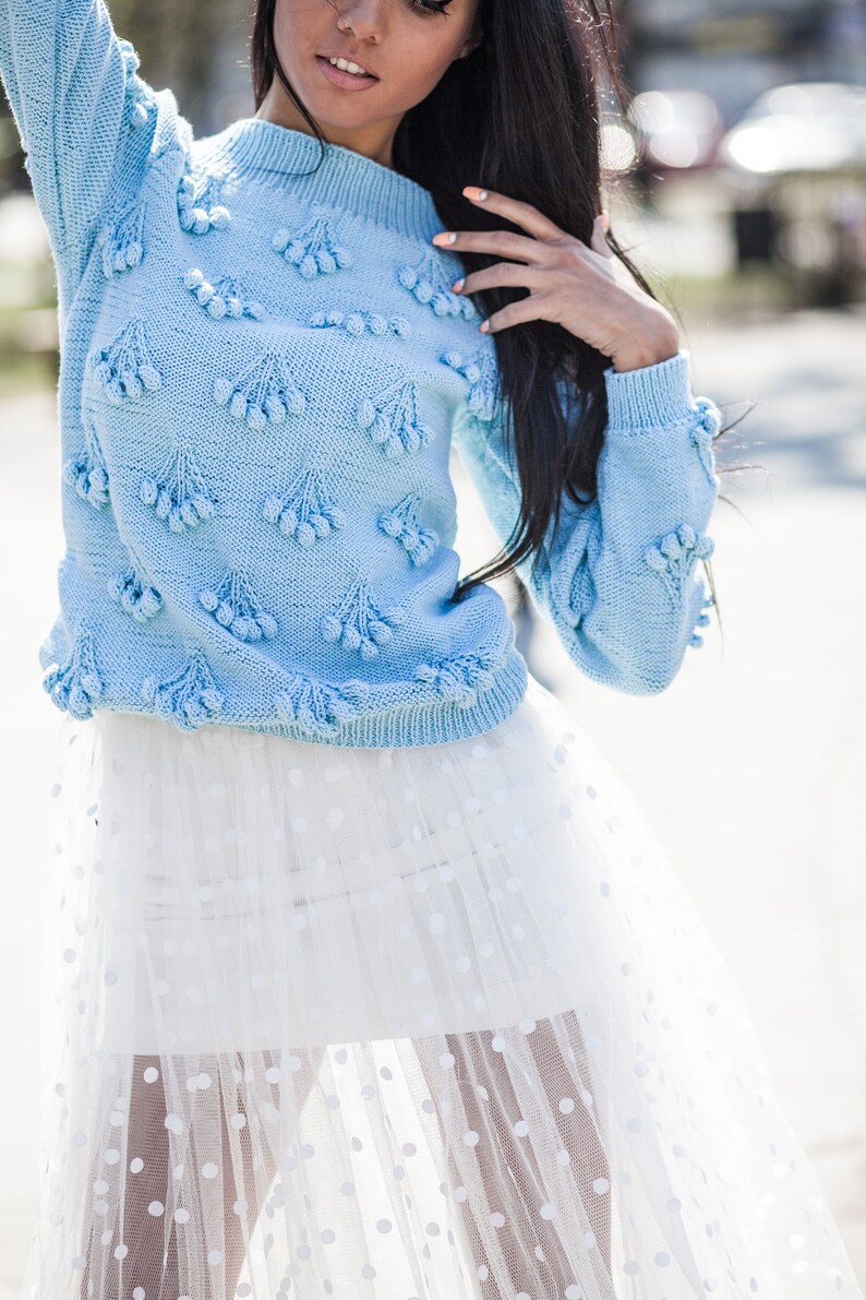 May include: A light blue knitted sweater with pom-poms and a white tulle skirt with polka dots.