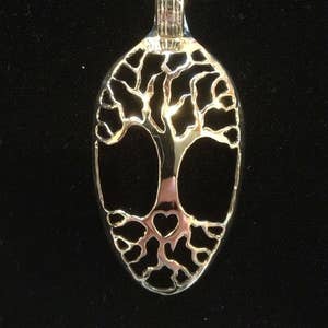 May include: A silver pendant necklace with a tree of life design. The pendant is shaped like a spoon and has a heart at the base of the tree.