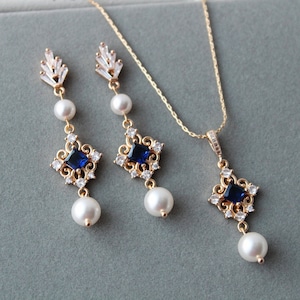 May include: A gold necklace and earrings set with a blue square gemstone pendant and pearl accents.