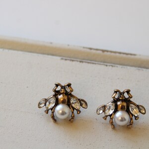 May include: A pair of gold tone bee earrings with clear crystal accents and a pearl center.