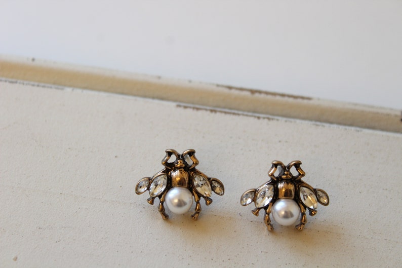 May include: A pair of gold tone bee earrings with clear crystal accents and a pearl center.