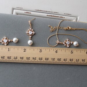 May include: A gold necklace and earrings set with a square pendant and pearl drop. The pendant is adorned with clear cubic zirconia stones. The necklace is 18 inches long and the earrings are 2 inches long.