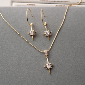 May include: A gold necklace and earrings set with a starburst pendant and matching earrings. Each piece features a clear oval-shaped stone in the centre.