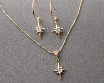 May include: A gold necklace and earrings set with a starburst pendant and matching earrings. Each piece features a clear oval-shaped stone in the center.