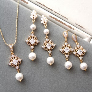 May include: A gold necklace and earrings set with a delicate chain, a square pendant with clear stones, and a pearl drop. The earrings have a similar design with a square pendant and a pearl drop.