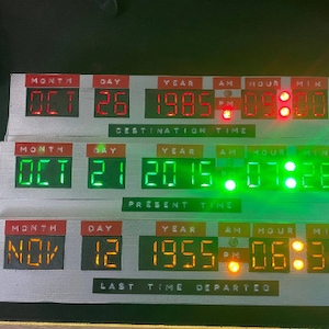 Peut inclure: Un appareil de voyage dans le temps de réplique avec trois écrans numériques affichant des dates et des heures. L'écran supérieur affiche "OCT 26 1985 09:00 PM". L'écran du milieu affiche "OCT 21 2015 07:28". L'écran inférieur affiche "NOV 12 1955 06:38".
