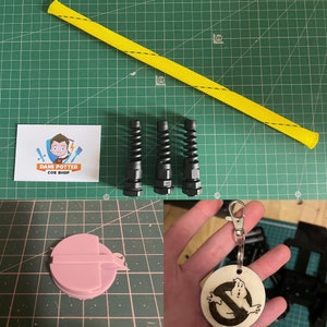 May include: Cosplay accessories including a yellow braided tube, three black spring connectors, a pink plastic component, and a wooden Ghostbusters keychain. A business card with a cartoon logo is also visible.