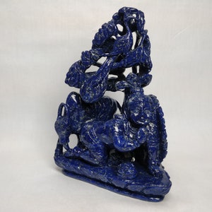 May include: A blue lapis lazuli sculpture of a kneeling figure with a tree behind it. The sculpture is intricately carved and has a detailed design.