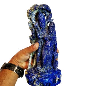 May include: A blue lapis lazuli sculpture of the Hindu deities Krishna and Radha. The sculpture is intricately carved and features a tree behind the figures.