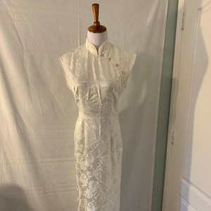 May include: A white sleeveless dress with a mandarin collar and a floral pattern. The dress has a fitted bodice and a flowing skirt.
