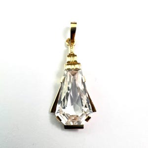 May include: A gold-colored pendant with a clear, faceted, teardrop-shaped crystal. The pendant has a rectangular top loop and geometric accents. The crystal is approximately 1.5 inches long.