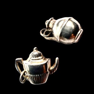 Peut inclure: Deux breloques en métal argenté sur fond noir. L'une est une théière avec anse et bec verseur. L'autre est une petite cruche. Les deux breloques ont une surface brillante et réfléchissante.
