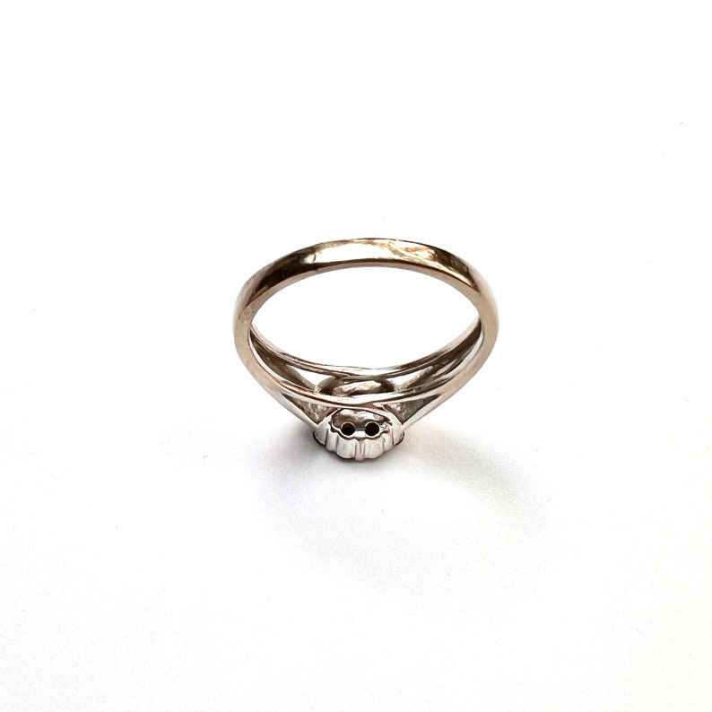 May include: A silver ring with a double band design. The ring features a small, round, possibly gemstone, center stone. The band has a split design near the center stone, creating an open, airy look. The ring is set against a white background.