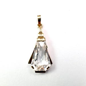 May include: A gold-toned pendant with a large, clear, faceted crystal. The crystal is teardrop-shaped with a pointed bottom and is framed by gold metal and dark accents. The pendant has a small loop at the top for a chain.