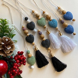 May include: Seven handmade lava stone heart ornaments with wooden beads and tassels. The hearts are in shades of green, blue, and black. The tassels are white, black, and green.