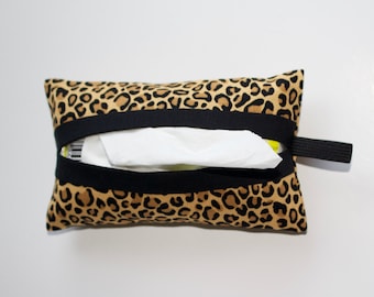 May include: A rectangular tissue holder with a leopard print pattern. The holder is made of fabric with black elastic bands and a black elastic loop. White tissues are visible inside the opening.