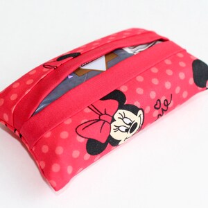 May include: A rectangular tissue holder featuring a red fabric with white polka dots and a Minnie Mouse design. The holder has a red band across the top and a slot for tissue dispensing.